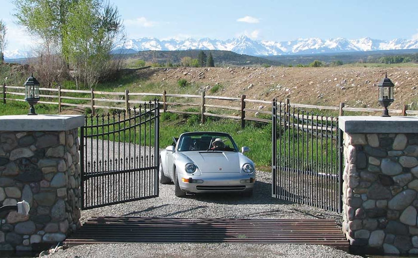 A Porsche driving through an open iron gate with mountains in the background
